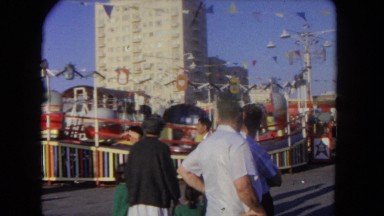 1962: two mature men and a woman socialize in front of a carnival ride