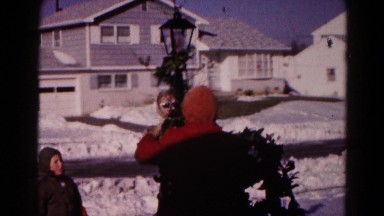 1959: a family outdoor in the snow decorating a light post for christmas