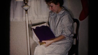 1959: a woman in a nightgown seated on a chair opening a gift on christmas