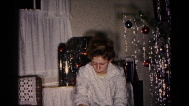 1959: a young woman sits beside a christmas tree calmly opening a large present.