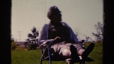 1962: an elderly woman sits in a lawn chair in a grassy area on a chilly day