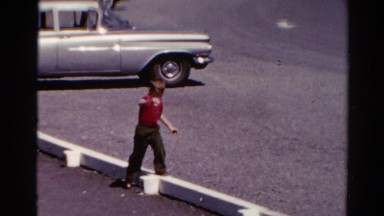 1962: a funny boy in red and black dress trying to walk along narrow blocks