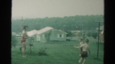 1962: an adult woman and two children play happily with a water sprinkler