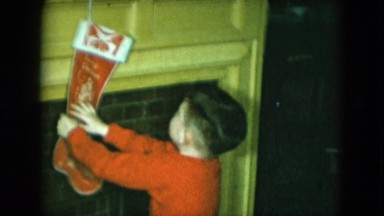 1951: young child in pajamas touches holiday stocking and motions at camera