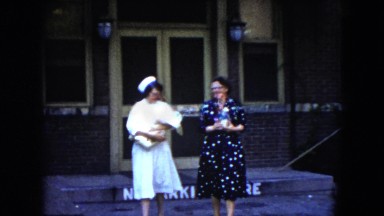 1951: nurse and woman carry new swaddled baby out of hospital to show friends