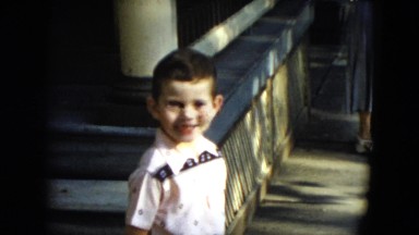 1951: a cute young boy in a white short standing on the sidewalk smiling