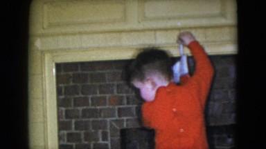 1951: a little boy in red pajamas tries to hang his stocking over the fireplace