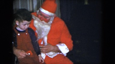 1951: a small dark haired boy sits on the lap of a man dressed as santa claus