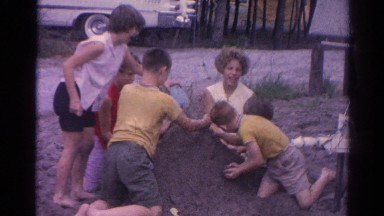 1962: a group of children play in the dirt next to a road in the summer