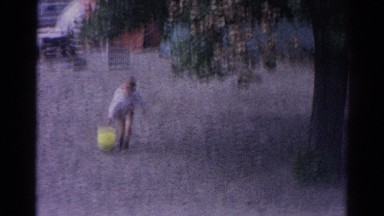 1962: a young boy carrying a heavy yellow bucket of water through the sand