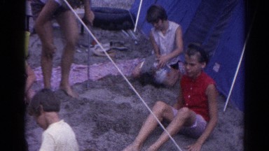 1962: various people including children gathered outdoor a tent in the sand