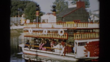 1957: passengers leisurely ride paddle-wheel boat along shore of calm lake