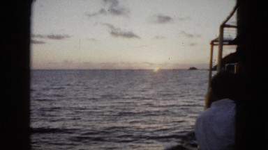 1962: view from a boat on the open ocean of the sunset and a nearby mountain