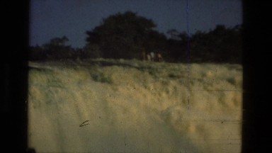1979: People Standing at Cascading Waterfall with Trees Above and Water