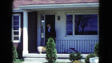 1959: man wearing suit exiting front door of house and greeting dog ARIZONA