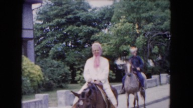 1961: a woman and a man ride on horseback with a boy following them on a bicycle
