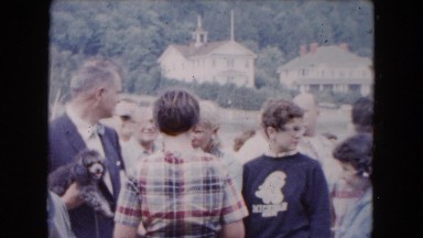 1961: a man is holding a dog while people are standing outdoor. MICHIGAN