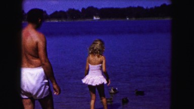 1961: father with two girls watch carefully as they wade in shallow water