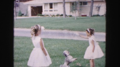 1961: two girls in white dresses and gloves playing with dog in yard MINNESOTA