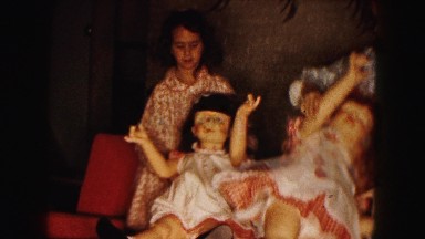 1961: two girls dressed in night clothes play with large dolls seated in chairs