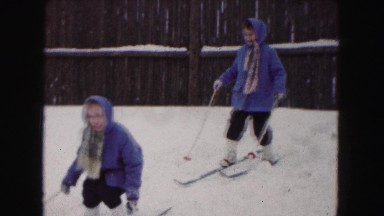 1961: two girls dressed in matching coats and pants cross country ski in a snow