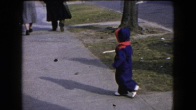1954: adorable young child bundled up in snowsuit tries to find footing
