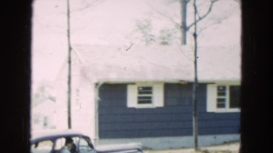 1954: a woman holding a child while standing in the yard in front of a house