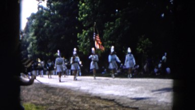 1955: a group of young parading with the american flag on a road in a rural area