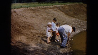 1955: dad digging at the edge of a pond while three small children watch