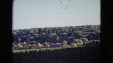 1958: a hilly remote green landscape with structures under a blue sky NEVADA