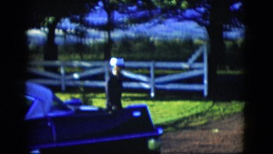 1958: a well dressed woman in a white hat walking around a car in the driveway