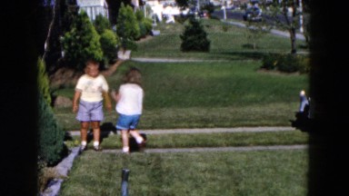1955: young girl and two young boys playing with metal slinky in yard