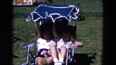 1955: two girls relax in the summer sharing a blue chair with a sunshade