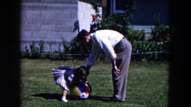 1955: small girl playing catch in green grassy yard with man