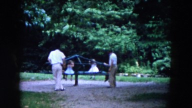 1955: adults watching children play on the merry-go-round in a park setting