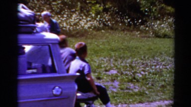 1964: little boys sit on the tailgate of a station wagon as people walk, talk