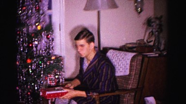 1967: a man dressed in pajamas and a robe sits and passes out holiday gifts