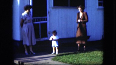 1951: two women stand and watch a toddler boy walk around and explore