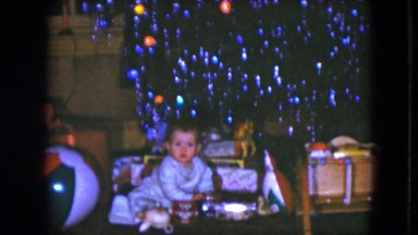 1951: baby plays with new toys and presents under tinseled tree on christmas