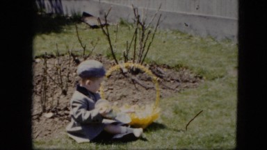 1951: a well dressed little boy sitting on the lawn playing with an easter egg