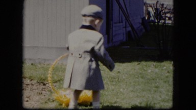 1951: a nice looking kid dressed in coat walking on the lawn with a doll