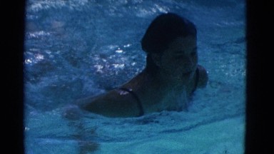 1953: a young woman swims through clear, blue water in a large pool