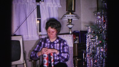 1967: a woman carefully opening a christmas gift in her lap HAGERSTOWN, MARYLAND