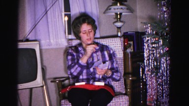 1967: a woman sitting beside a christmas tree is inspecting a present
