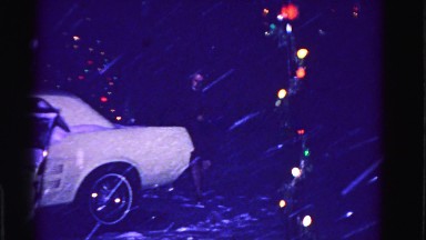 1967: a lady walks her dog which is wearing a sweater to the car in a snowstorm