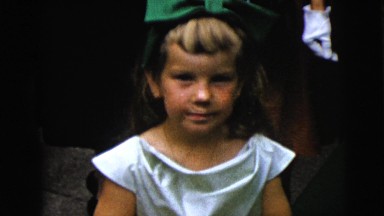 1962: a cute young girl with a dress and a wearing a big green bow in her hair