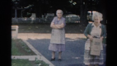 1964: old lady picking something from the ground watched by another one