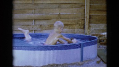 1968: a blonde haired and dark boy boy play around in a children swimming pool