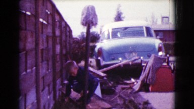 1968: a boy forages through junk and wreckage near a wall and a vehicle