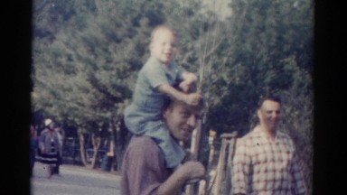 1962: a man outdoor smoking a cigarette with a toddler on his shoulders